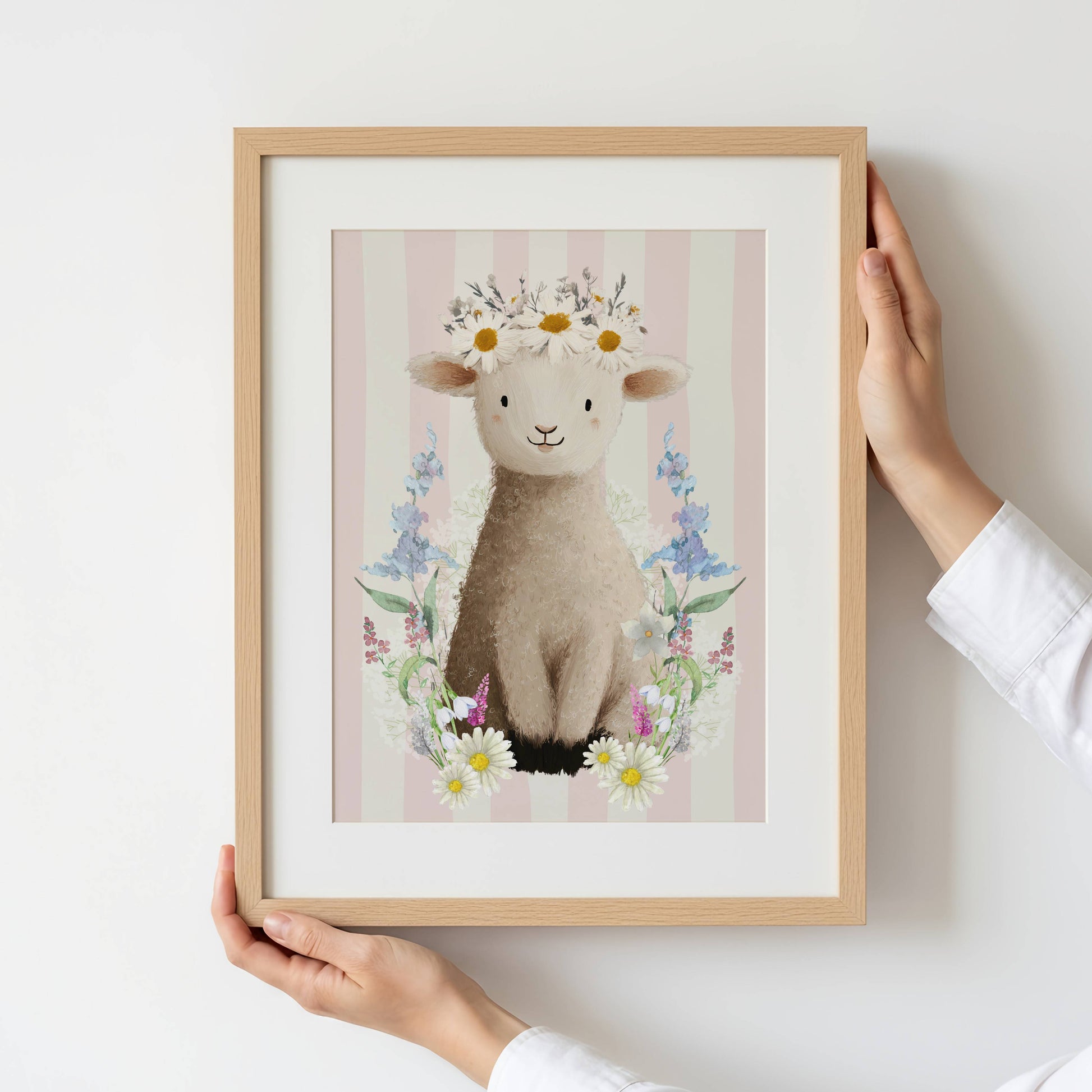 Framed artwork of a lamb with flowers held by a person against a white background
