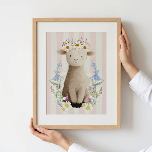 Framed artwork of a lamb with flowers held by a person against a white background