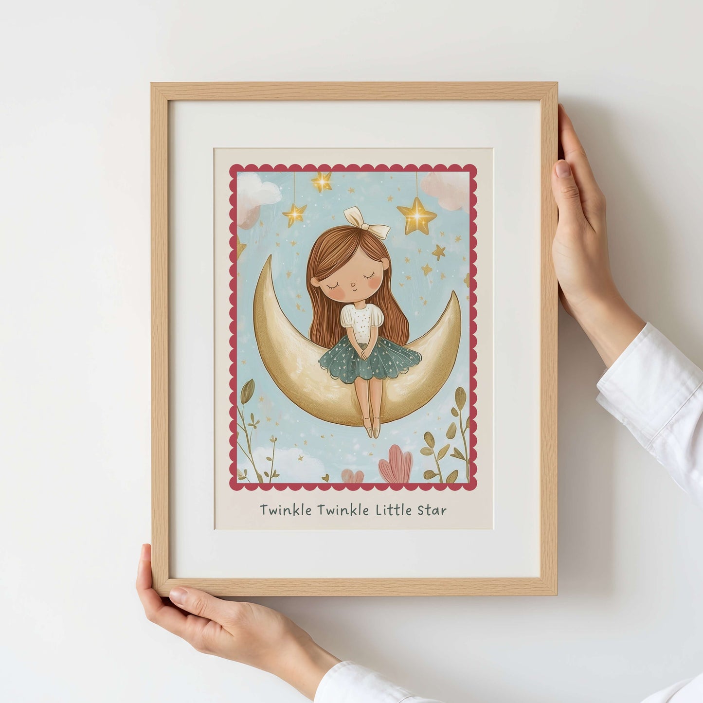 Framed artwork of a girl sitting on a crescent moon with stars and flowers, held by a person.